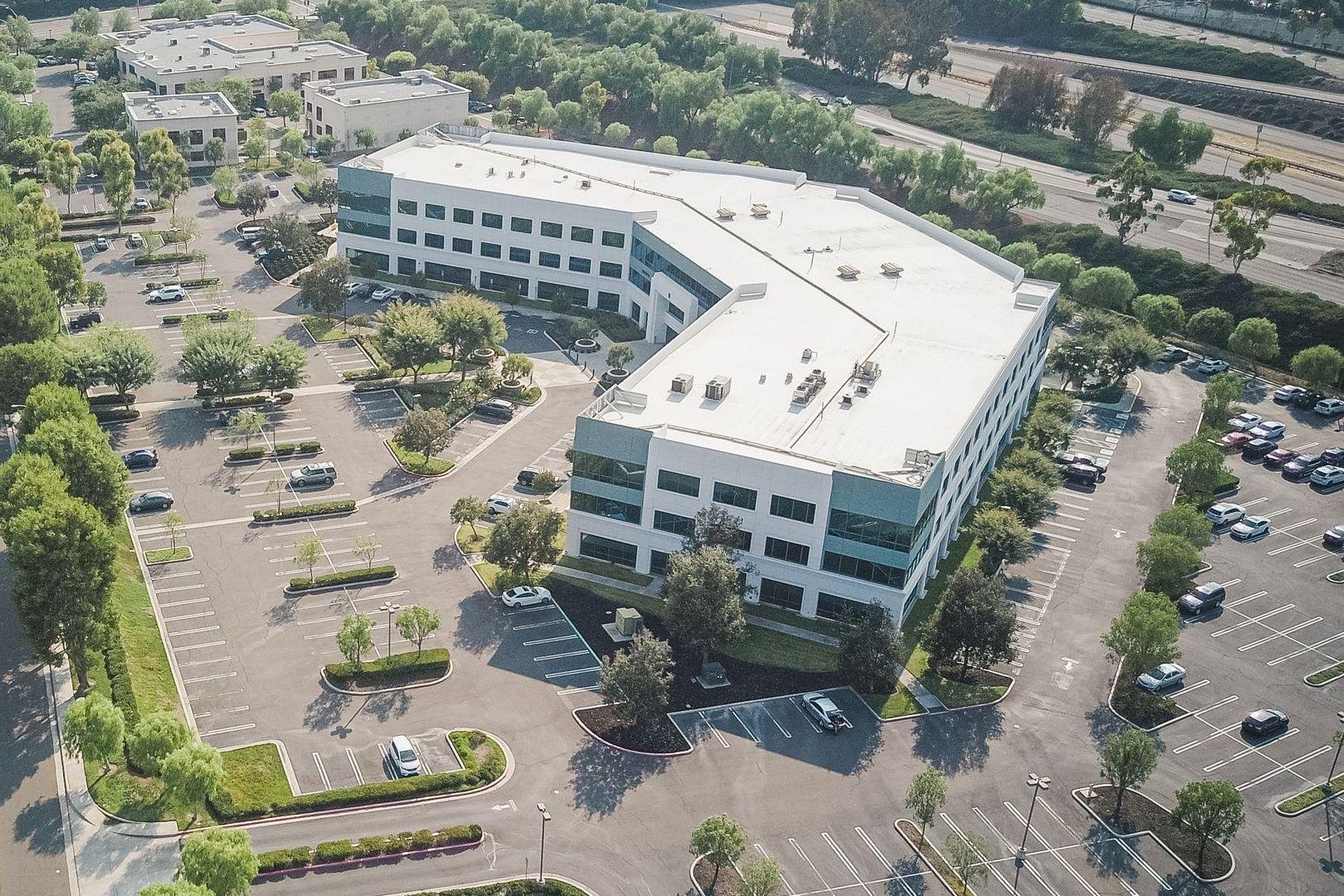 Aerial view of a three-story glass office building in a landscaped parking lot