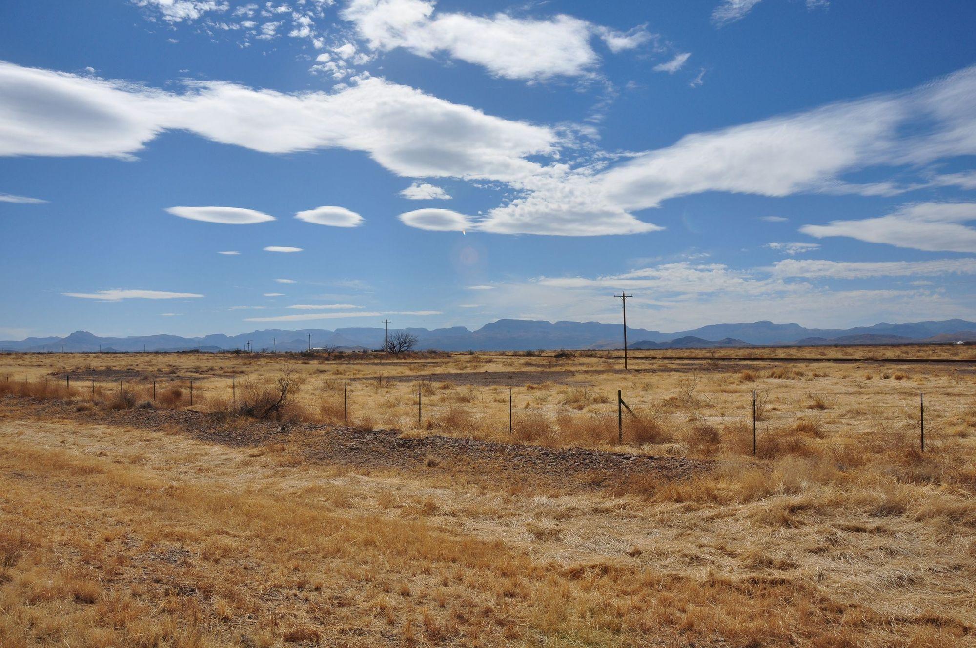 Open dry-grass acreage with a wire fence line and distant mesas