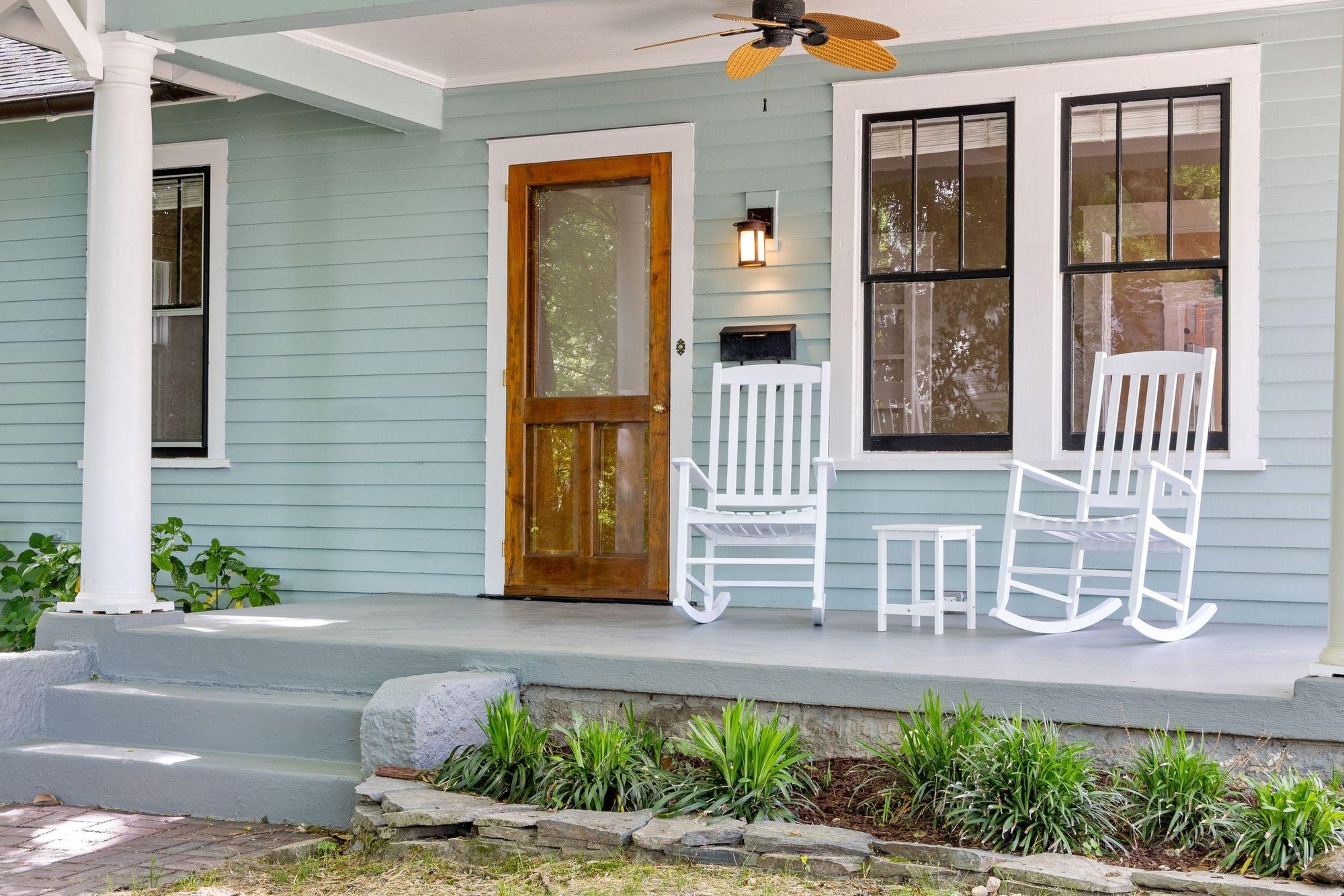 The front porch of a pale blue clapboard house with white rocking chairs