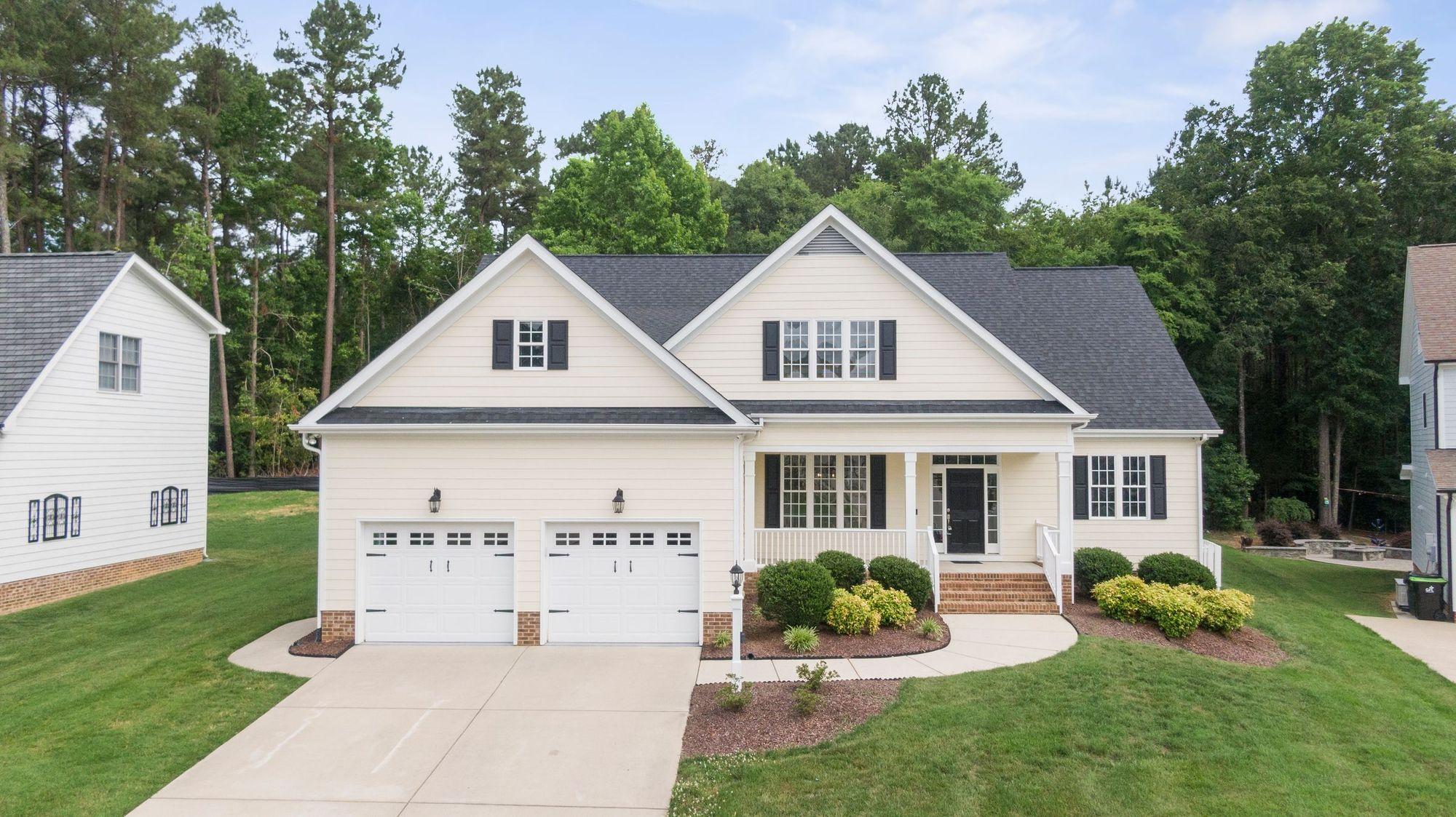 A cream two-story house with a two-car garage, a front porch and a lawn
