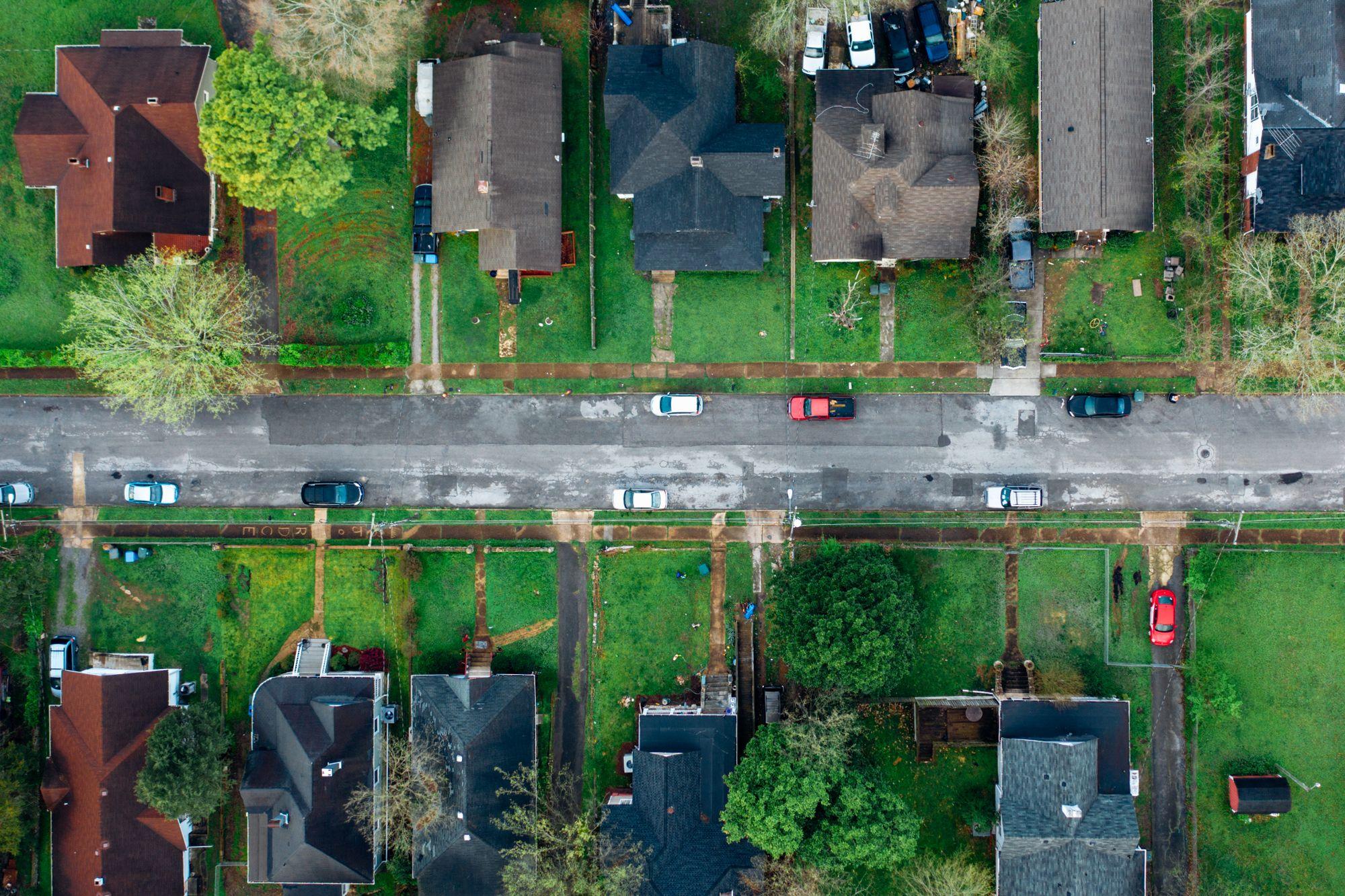 Aerial view of a residential street with houses, trees and parked cars on both sides