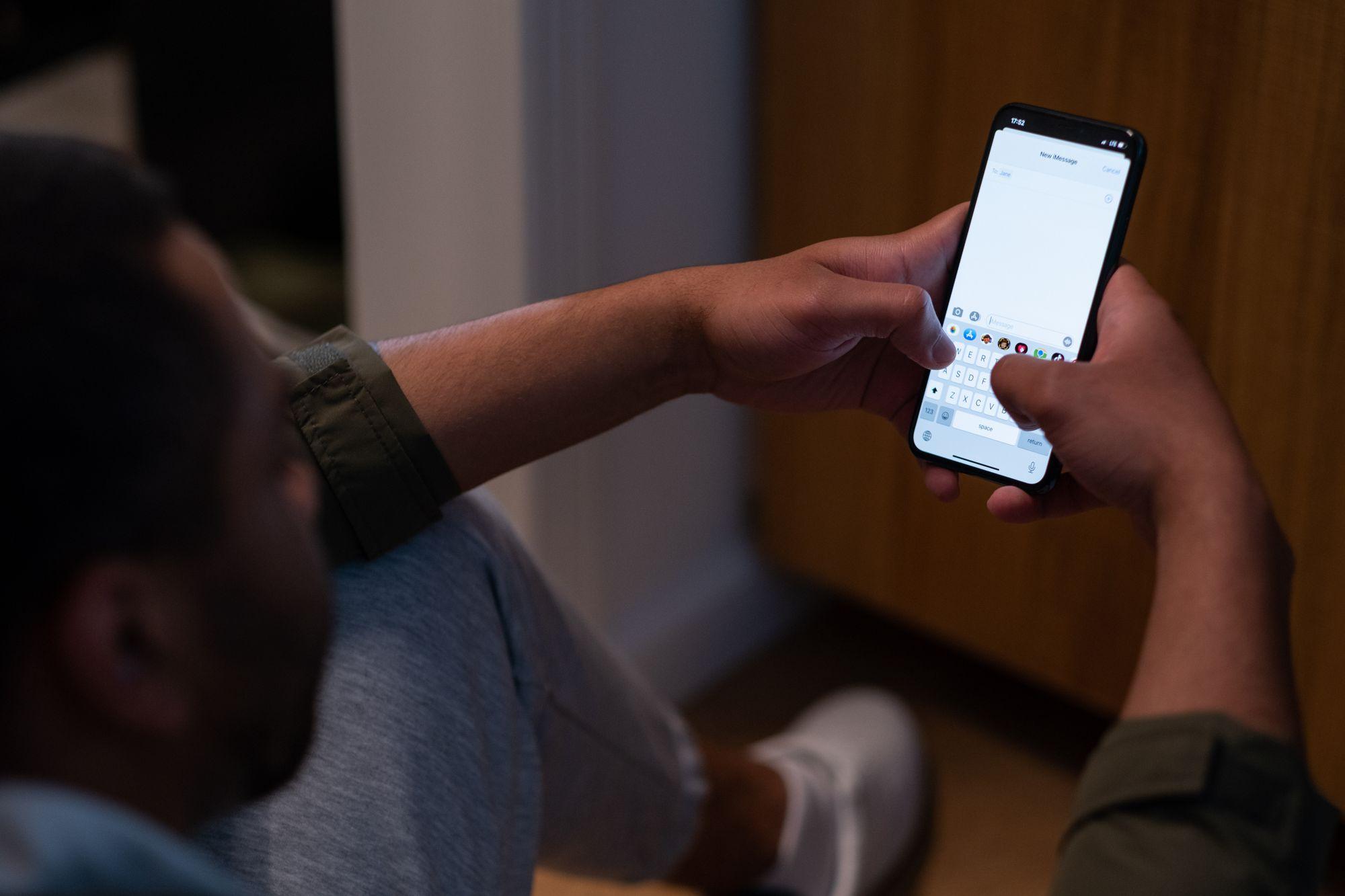 Close-up of a man typing a text message on his smartphone in a dim room