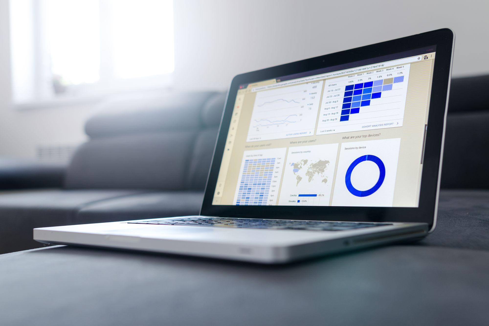 Open laptop on a gray sofa showing a dashboard of charts and tables