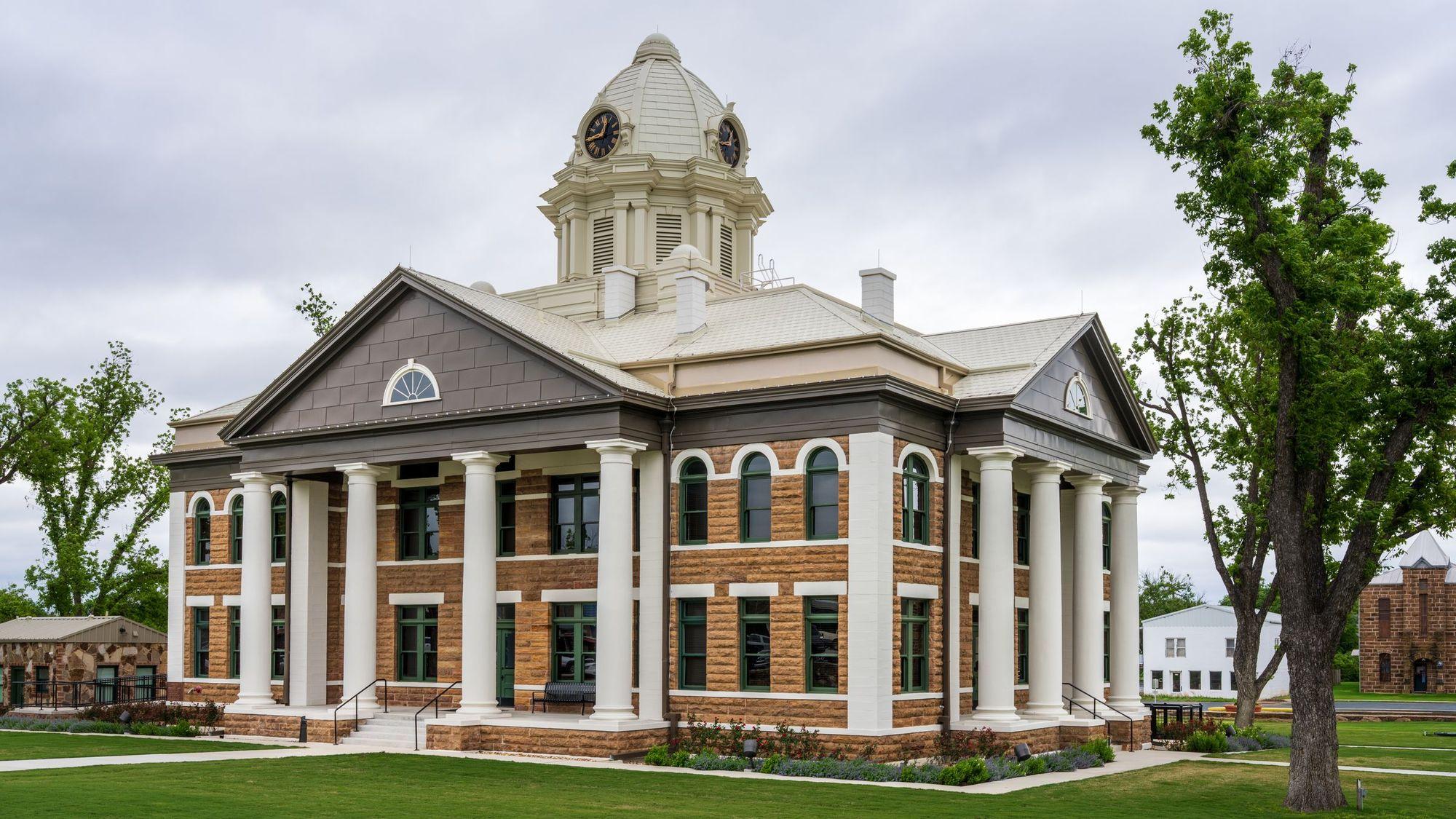 Historic sandstone county courthouse with white columns and a clock dome under an overcast sky