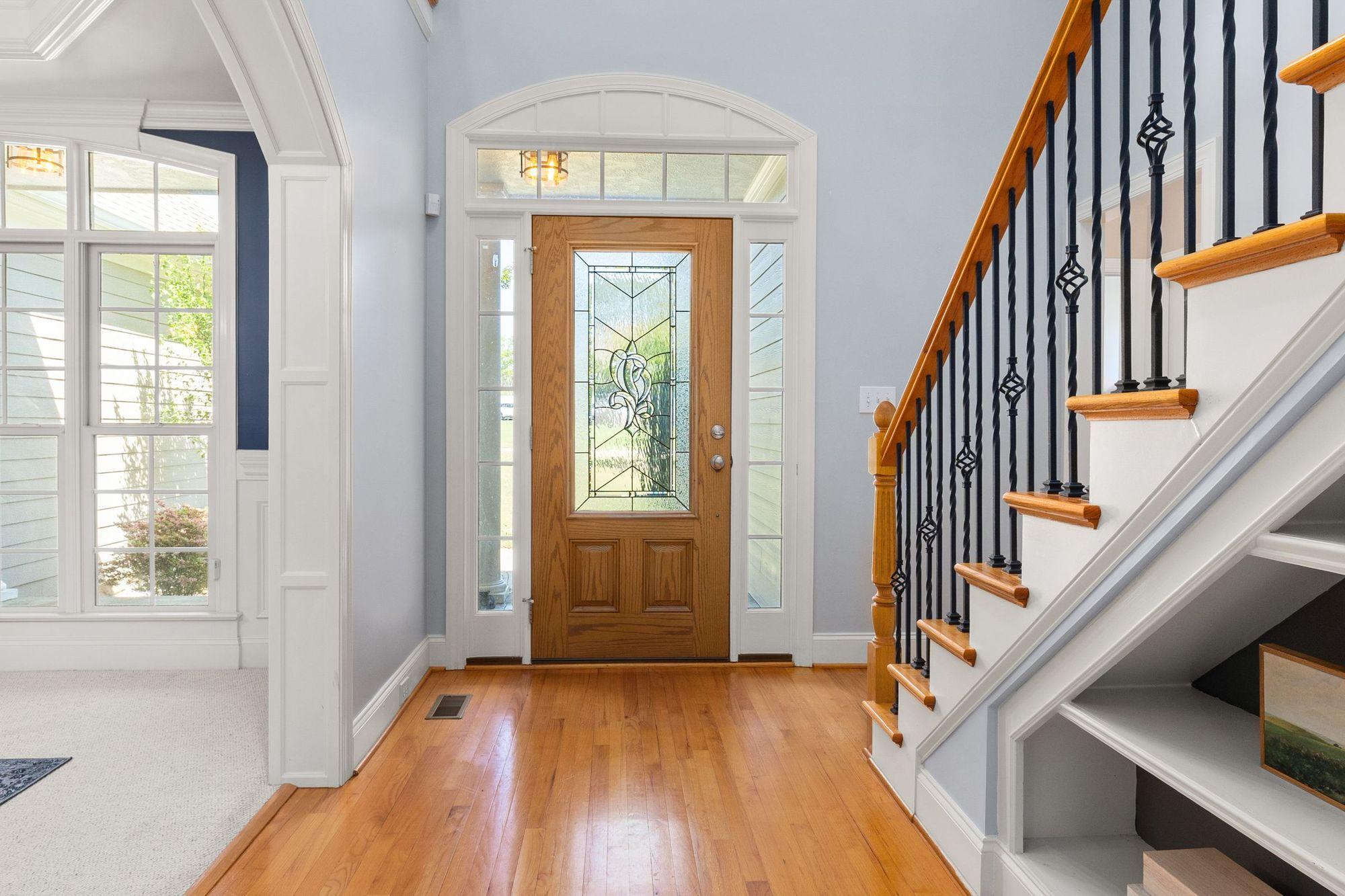 Sunlit home foyer with an oak front door, glass sidelights, hardwood floor and a staircase