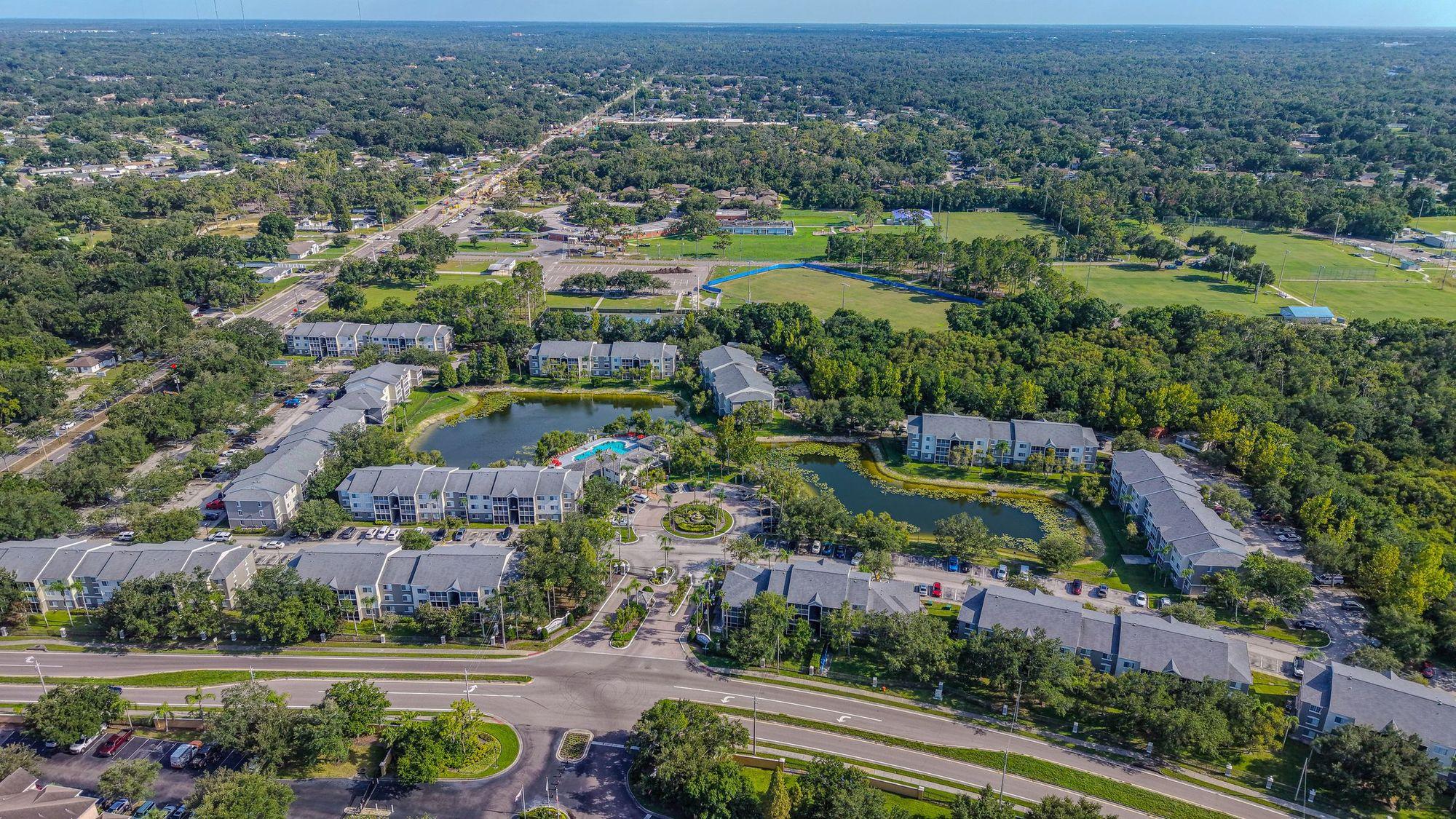 Aerial view of a three-story garden apartment complex with ponds, pool and trees in daylight