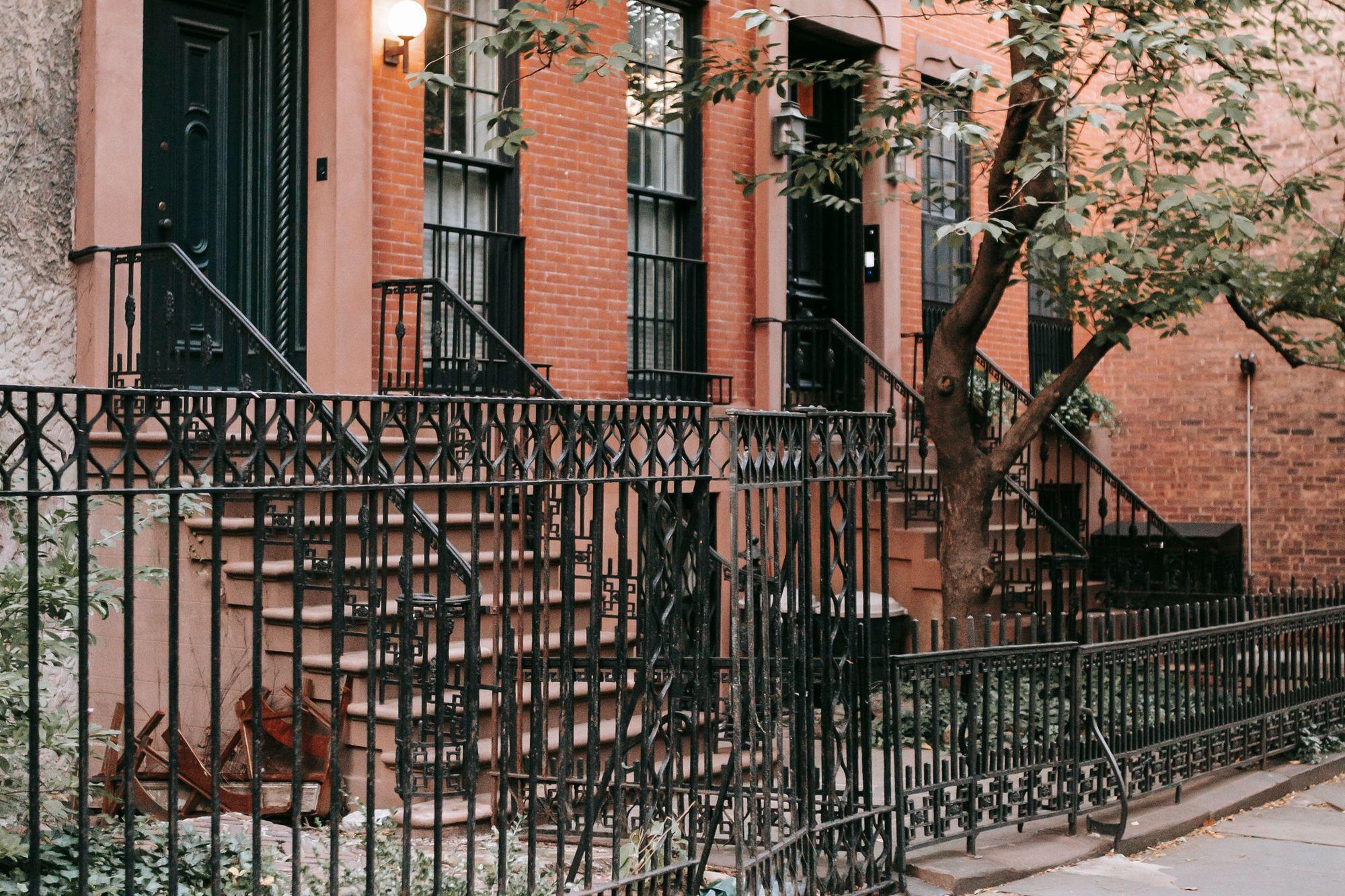 Brick rowhouses with iron stoop railings and a street tree
