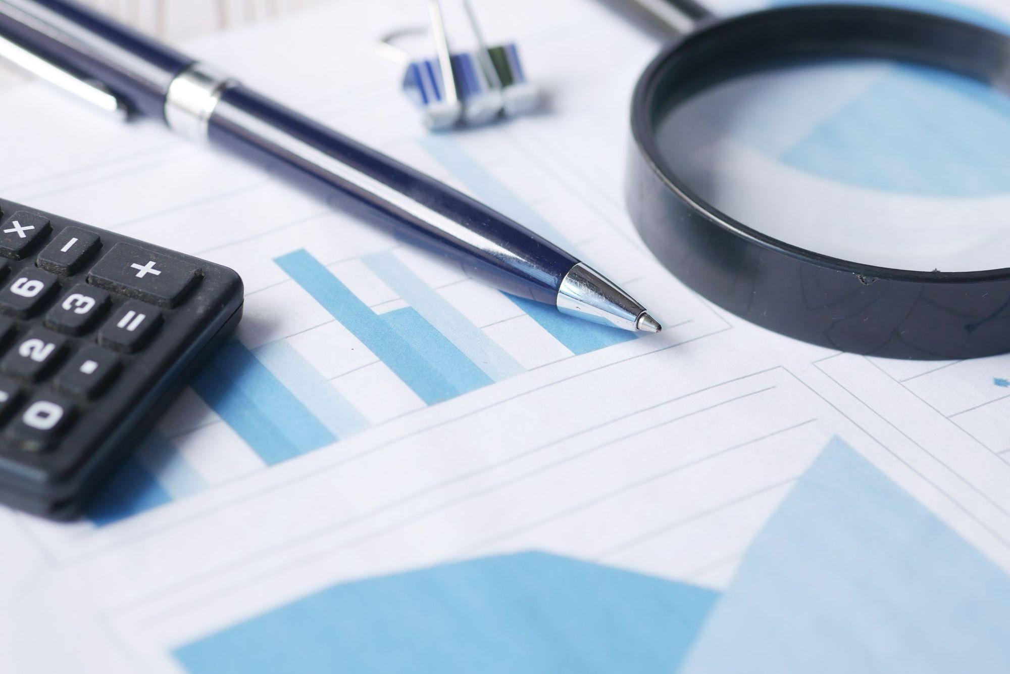 Calculator, pen and magnifying glass resting on printed blue chart paperwork