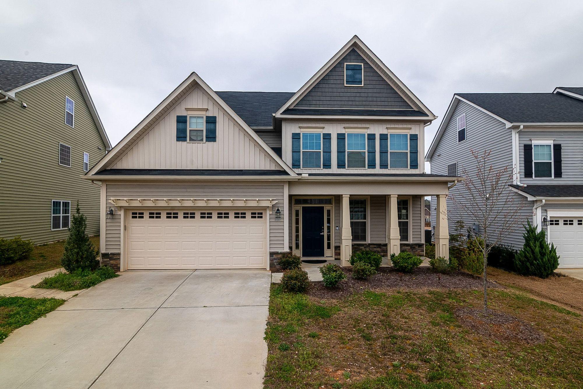 Two-story suburban house with closed blinds, empty driveway and patchy lawn under an overcast sky