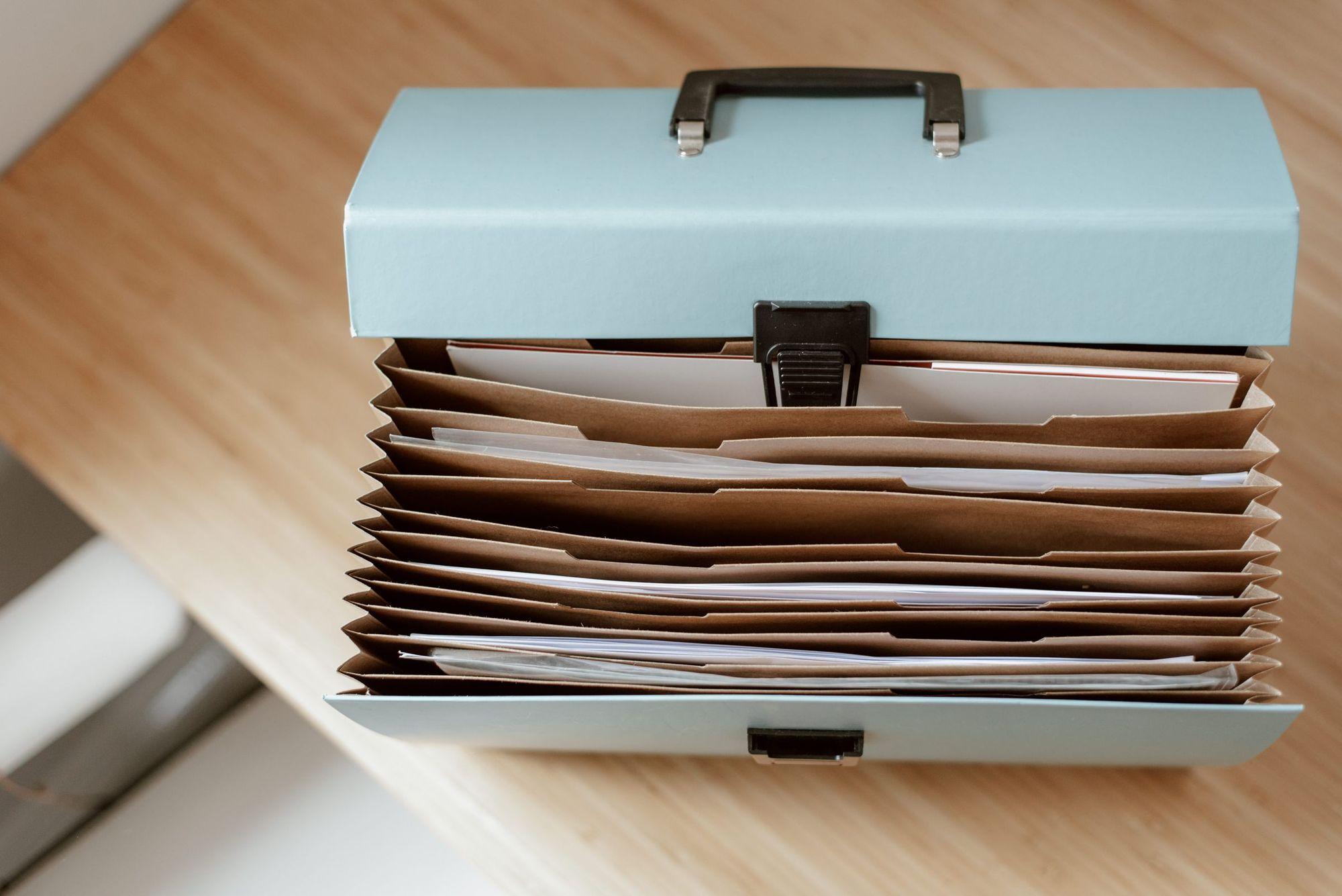 Open pale blue expanding file box with kraft folders and papers on a wooden desk